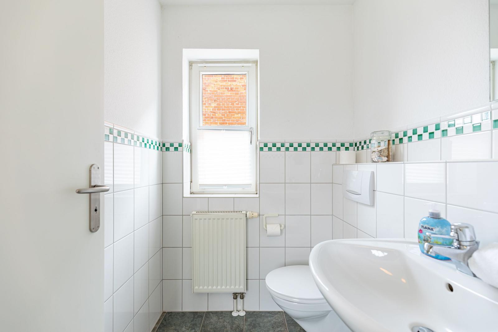 Badezimmer mit Toilette, Waschbecken und Fenster mit Blick auf Backsteinmauer.