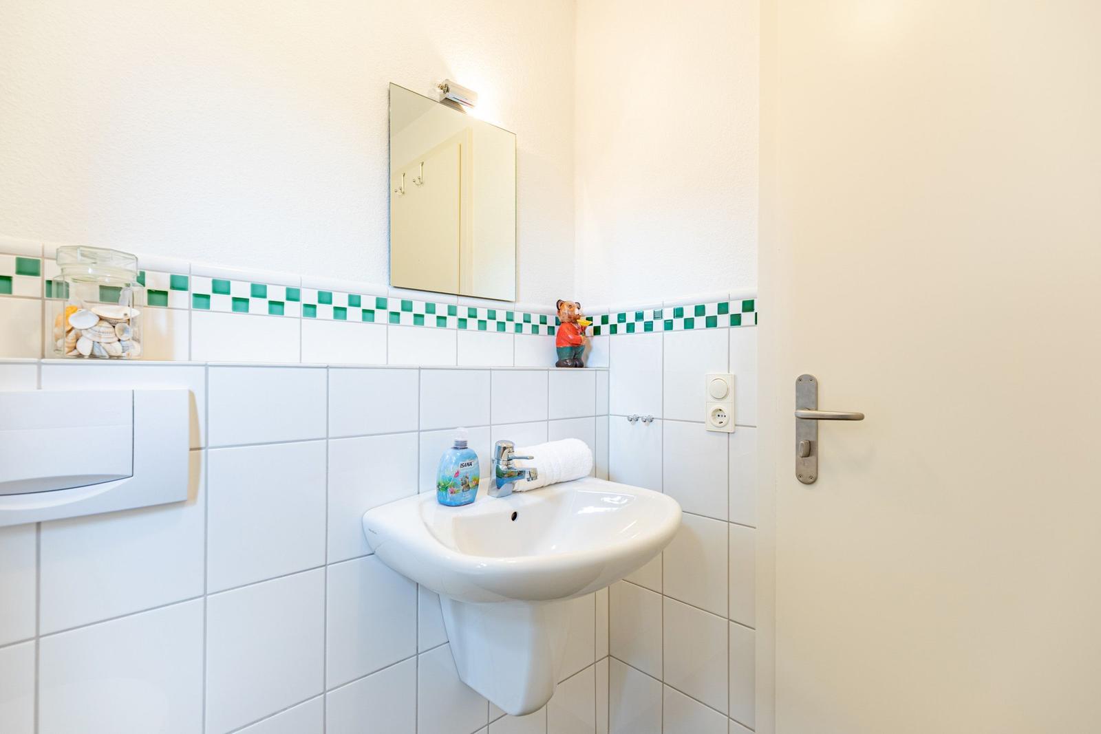 Badezimmer mit Waschbecken, Spiegel und grüner Fliesendekoration an der Wand.
