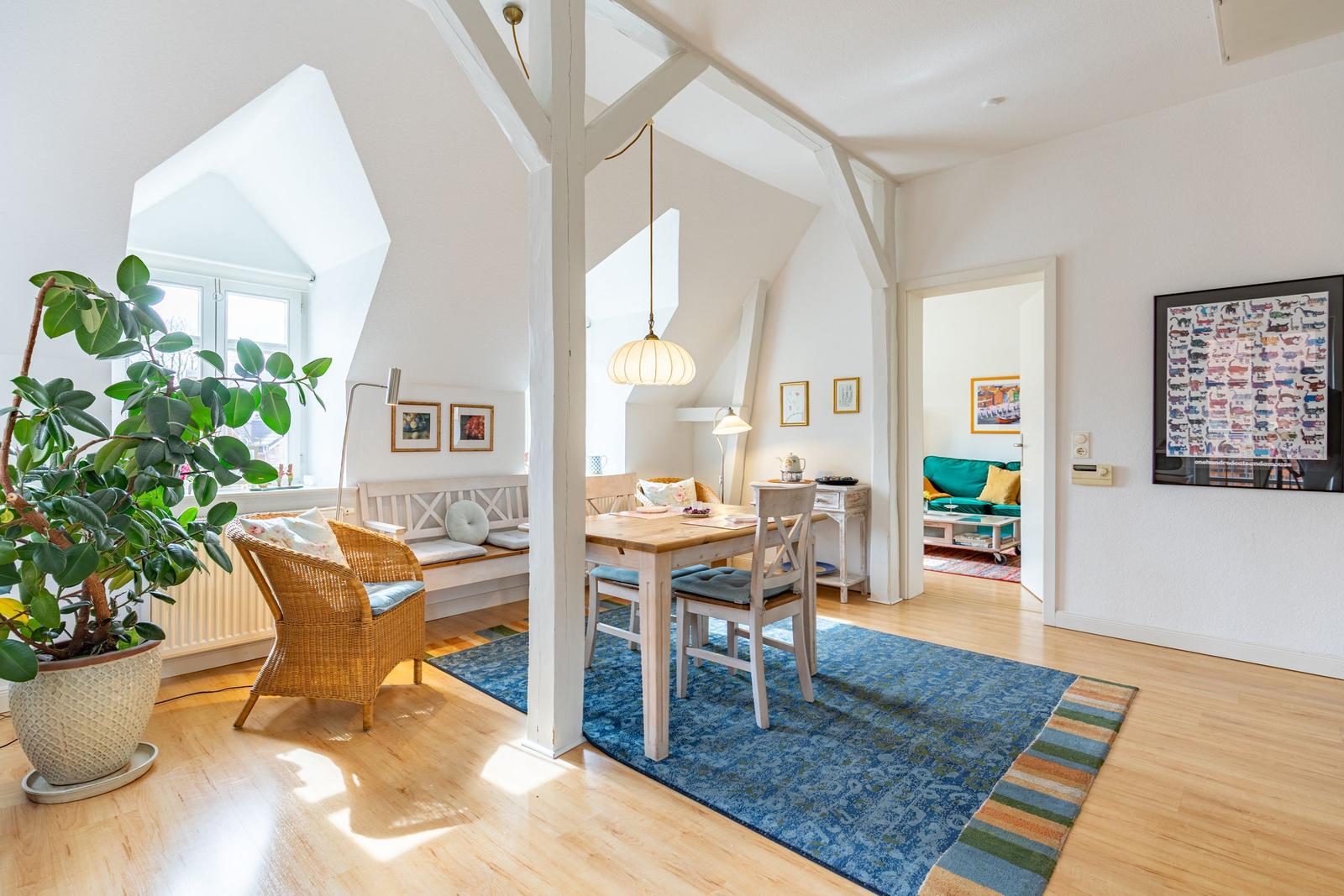 Wohn- und Essbereich mit Holzboden, Sitzgelegenheiten und Blick in das Schlafzimmer.