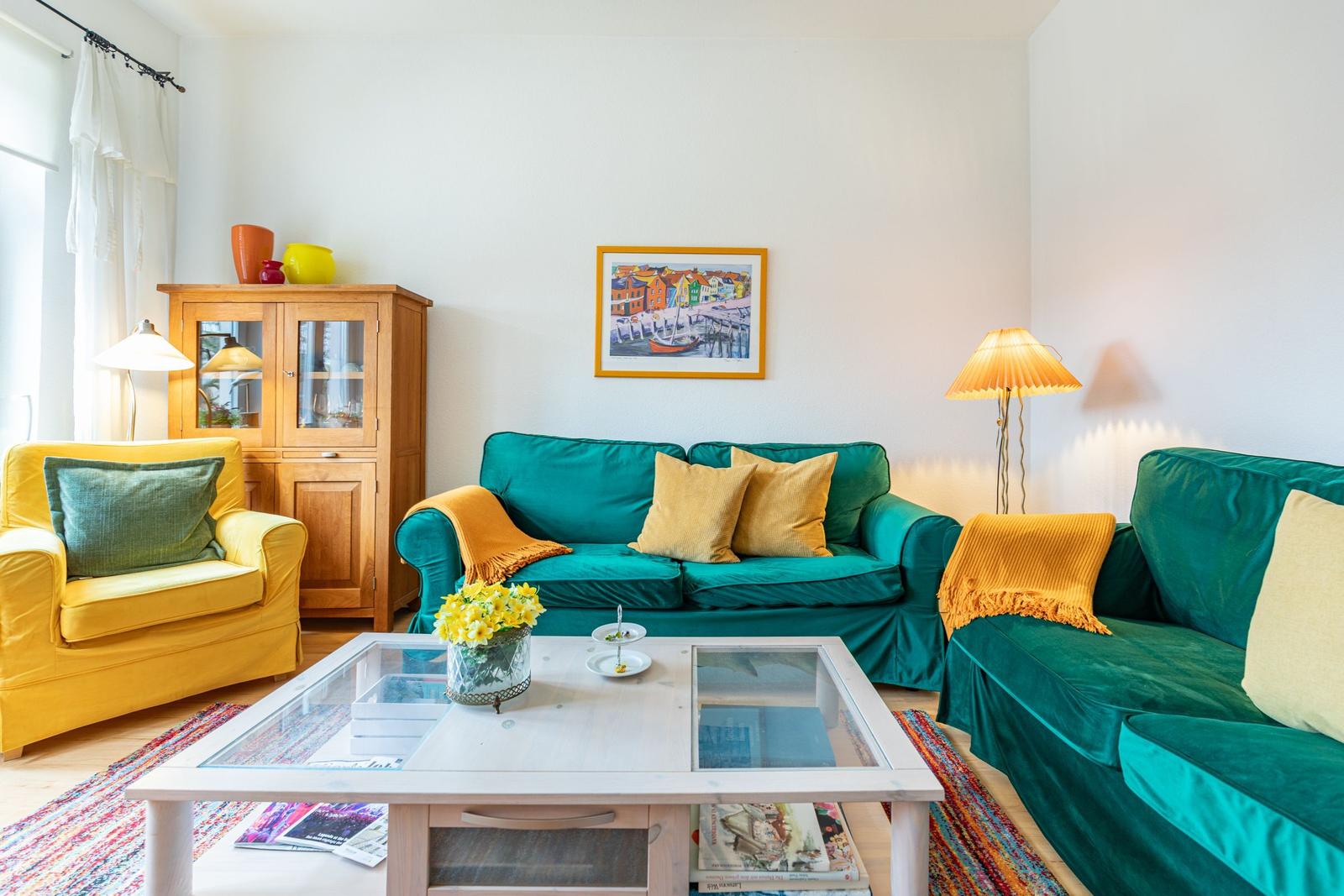 Ein Wohnzimmer mit grünen Sofas, einem gelben Sessel und einem Glas-Tisch.