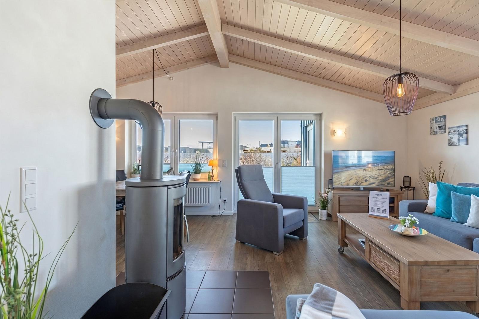 Wohnzimmer mit Holzdecke, Kamin, Sofa und TV. Blick auf Terrasse und Strand.