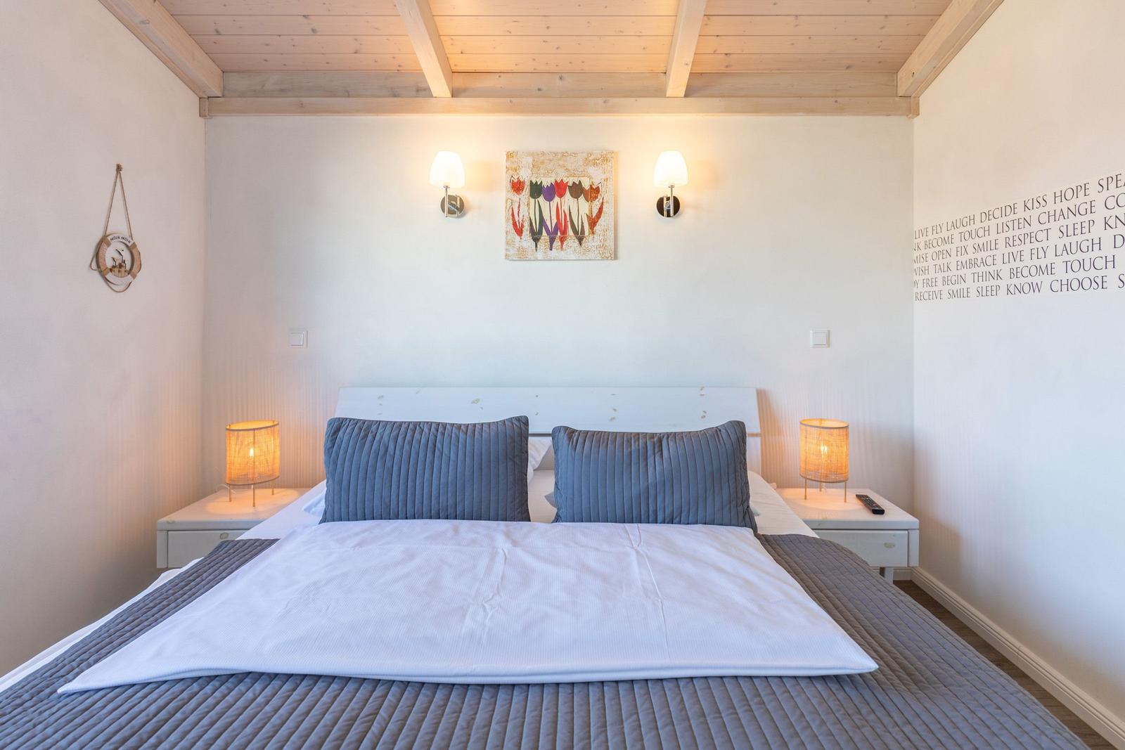 Schlafzimmer mit Bett, Nachttischen und Wandbild. Holzdecke und warme Beleuchtung.