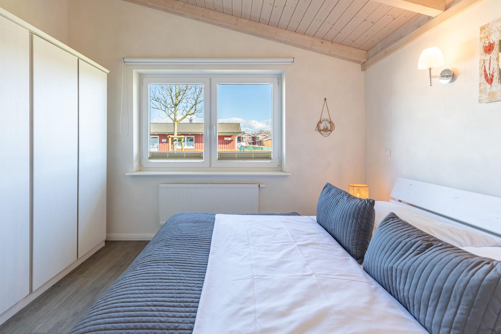 Schlafzimmer mit Bett, Fenster und Kleiderschrank. Blick auf rote Häuser.