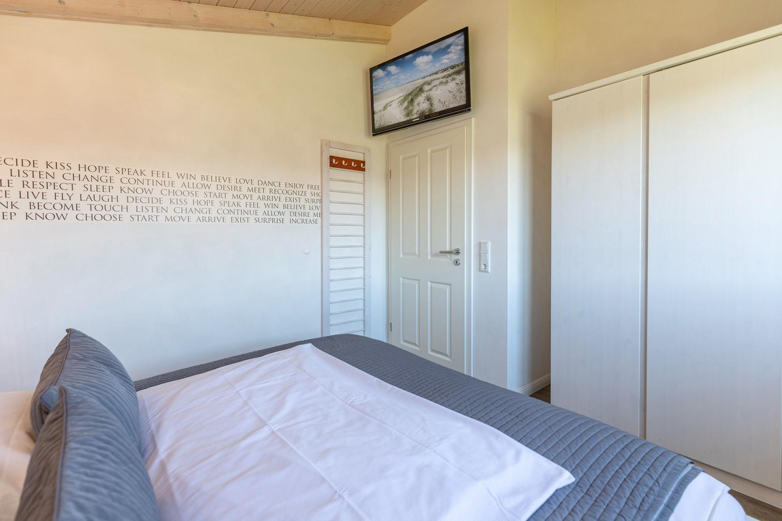 Schlafzimmer mit Bett, Kleiderschrank und Wandbild. Wand mit Aufschriften.