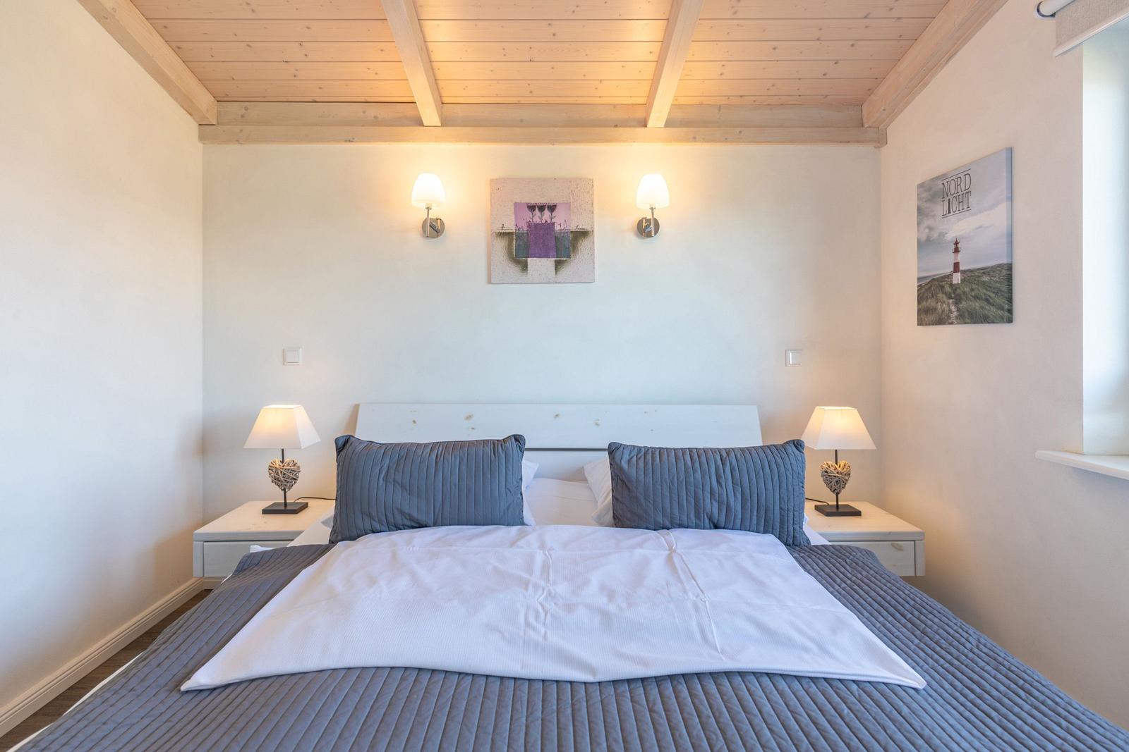 Schlafzimmer mit Bett, Nachttischen und Wandbildern. Holzdecke und Lampen.