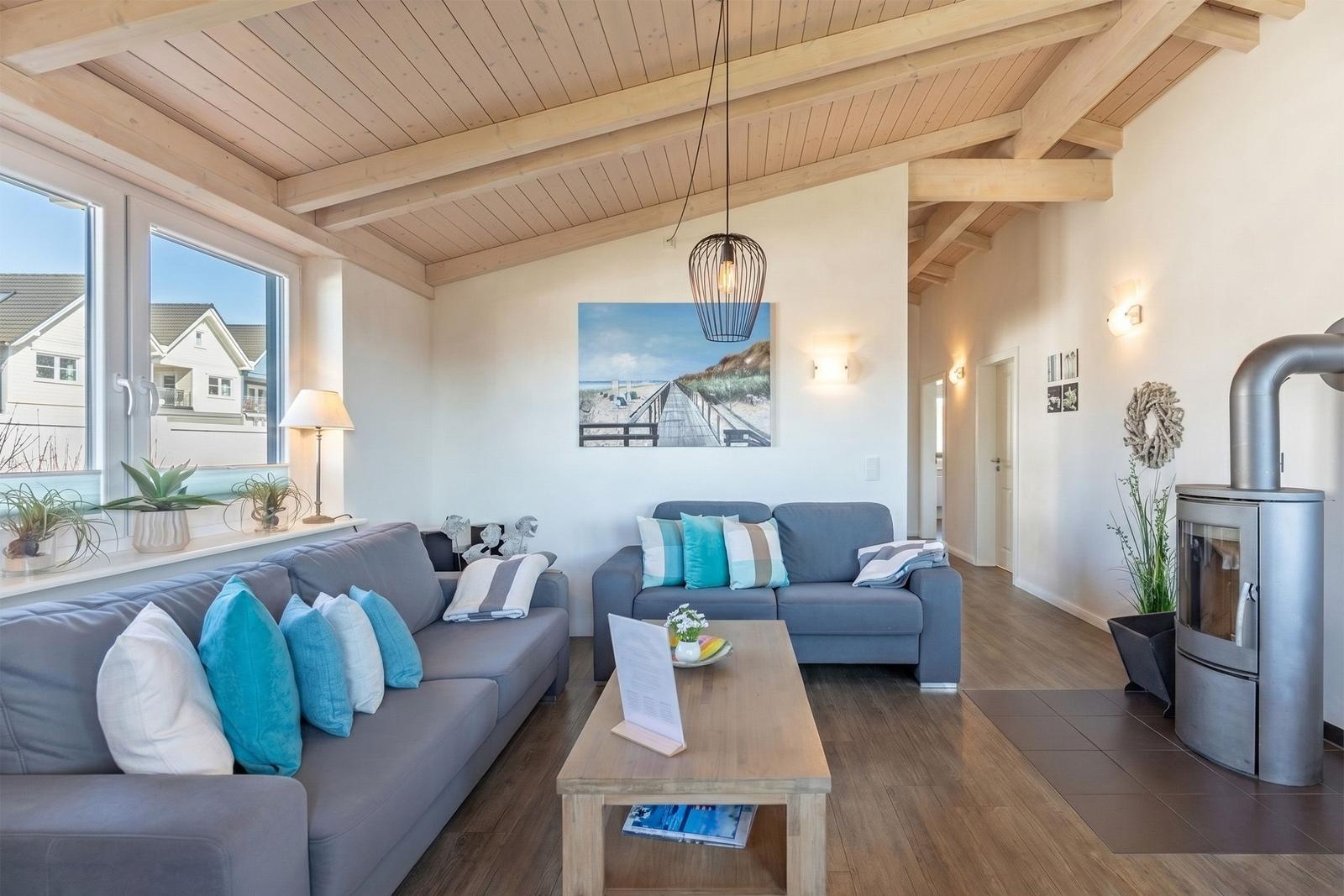 Wohnzimmer mit zwei Sofas, Holzdecke und Kaminofen. Fenster blicken auf Wohnhaus.