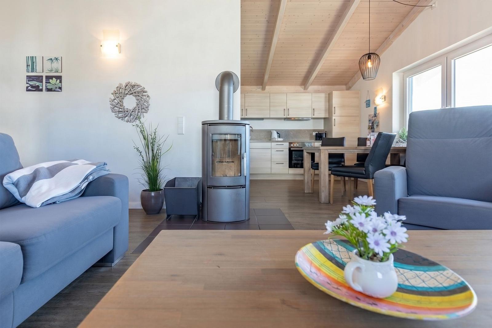 Wohnzimmer mit Kamin, Essbereich und Küche im Hintergrund. Holzdecke und moderne Einrichtung.