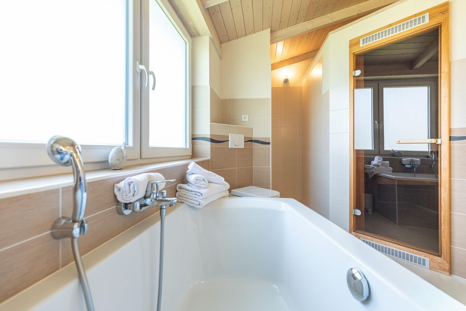 Bad mit Badewanne, Dusche und Fenster. Handtuchhalter und Duschbrause sind sichtbar.