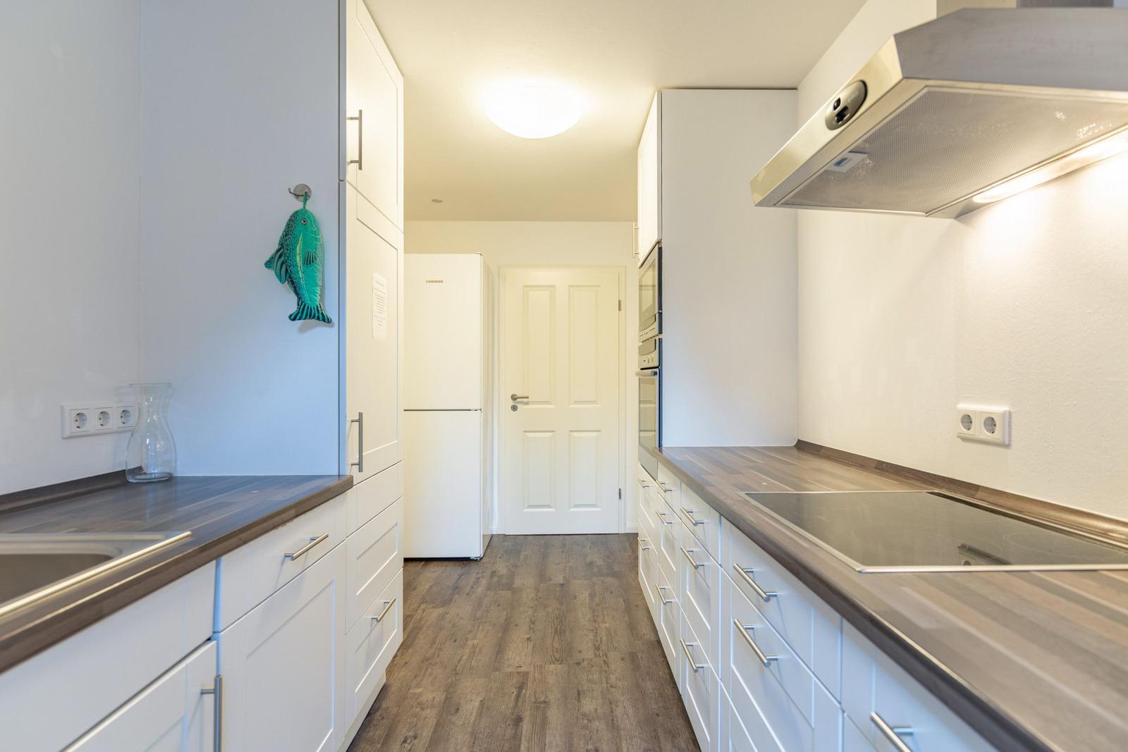 Küche mit weißen Schränken, dunklen Arbeitsplatten und Holzboden. An der Wand hängt ein grüner Fisch.