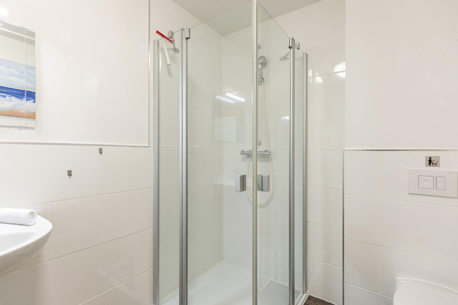 Badezimmer mit Dusche, Waschbecken und Toilette. Wand mit Bild und Fliesen.