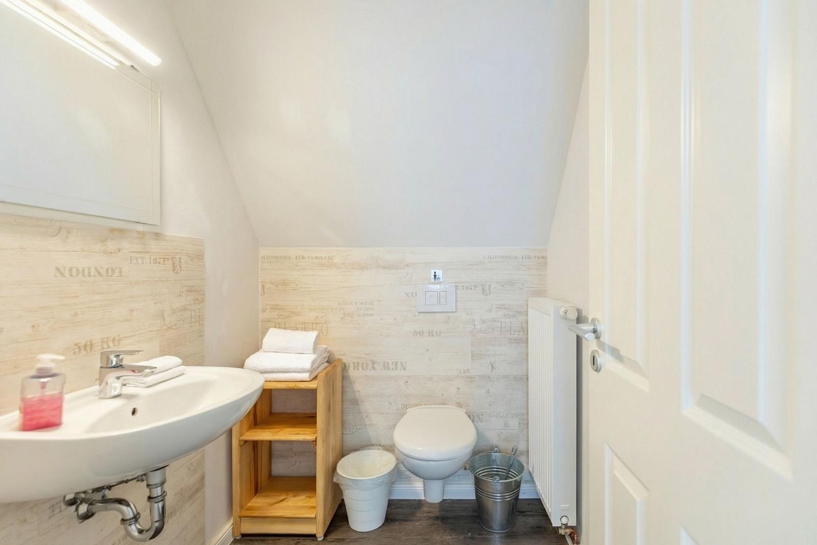Badezimmer mit Waschbecken, Toilette und Holzregal an der Wand.