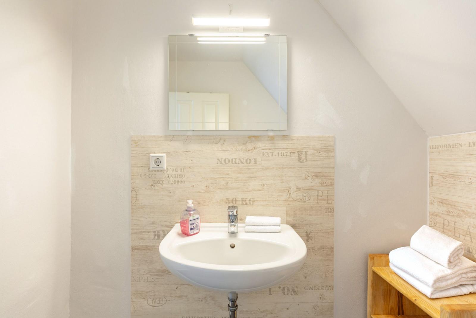 Badezimmer mit Waschbecken, Spiegel und Handtüchern an Holzwand