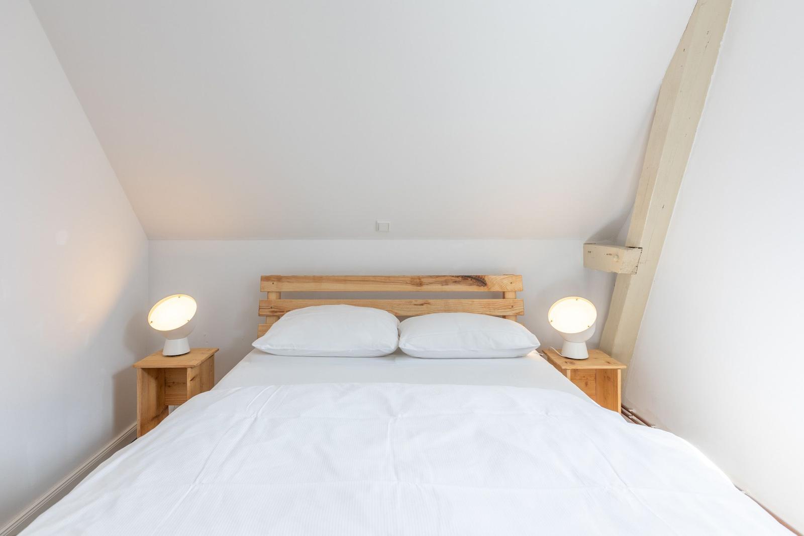 Schlafzimmer mit Bett, zwei Nachttischen und Lampen. Holzrahmen an der Wand.