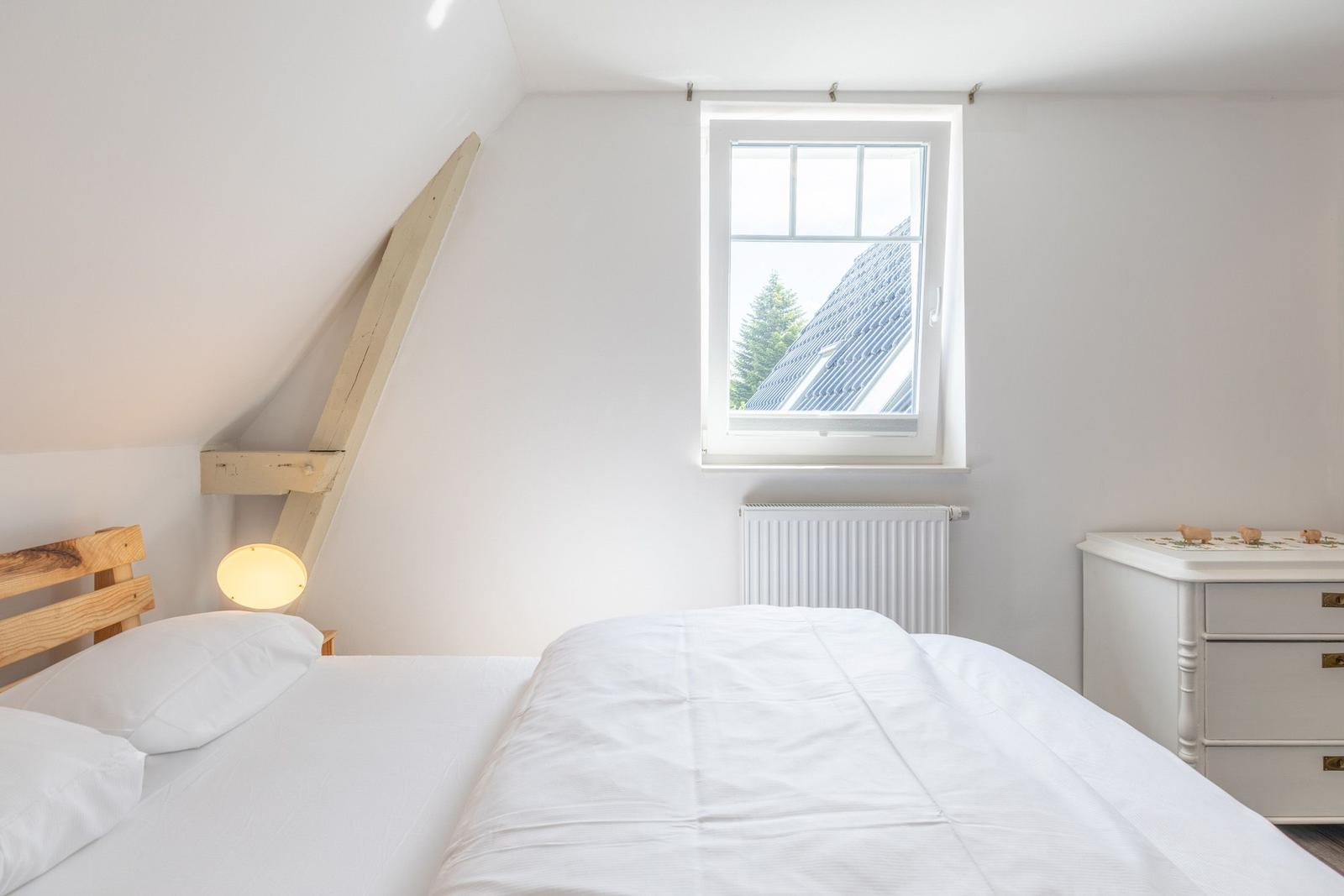Schlafzimmer mit Dachschrägen, Fenster und Bett.