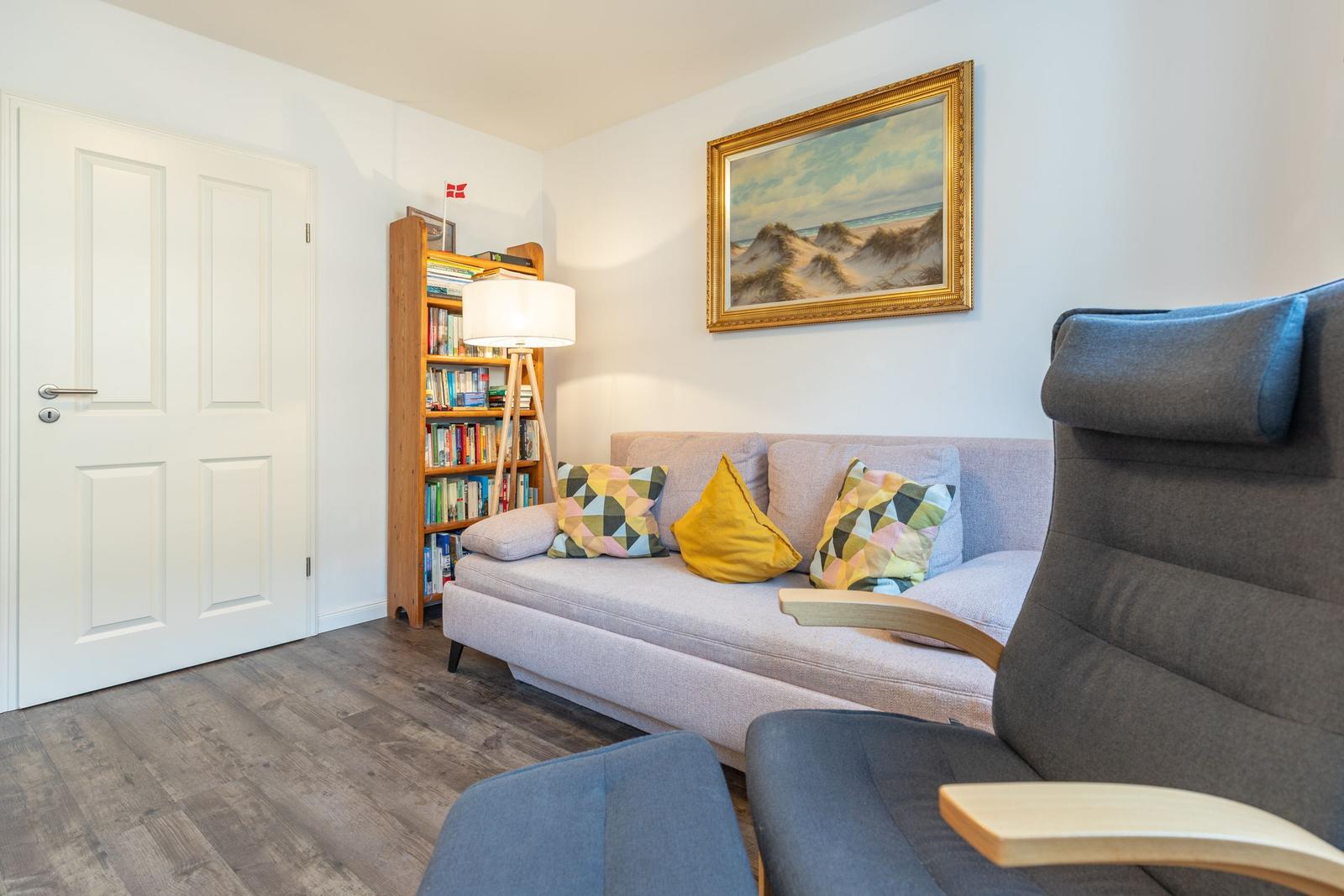 Wohnzimmer mit Sofa, Stuhl, Bücherregal und Wandbild