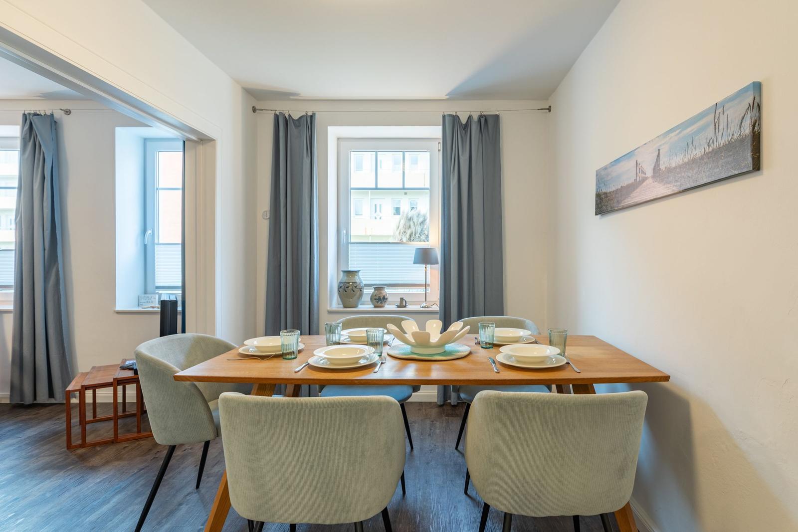 Esszimmer mit Holztisch, sechs Stühlen und Fenster mit Vorhängen.