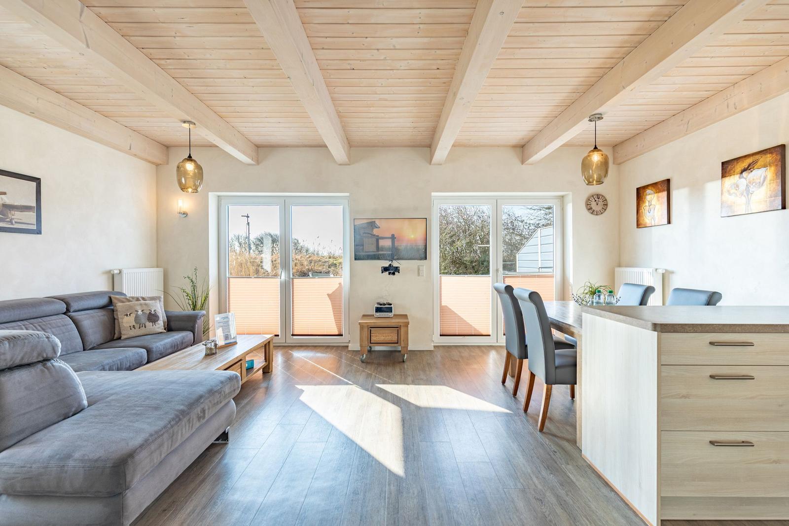 Wohn- und Essbereich mit Holzdecke, Sofa, Esstisch und Blick auf Balkon.
