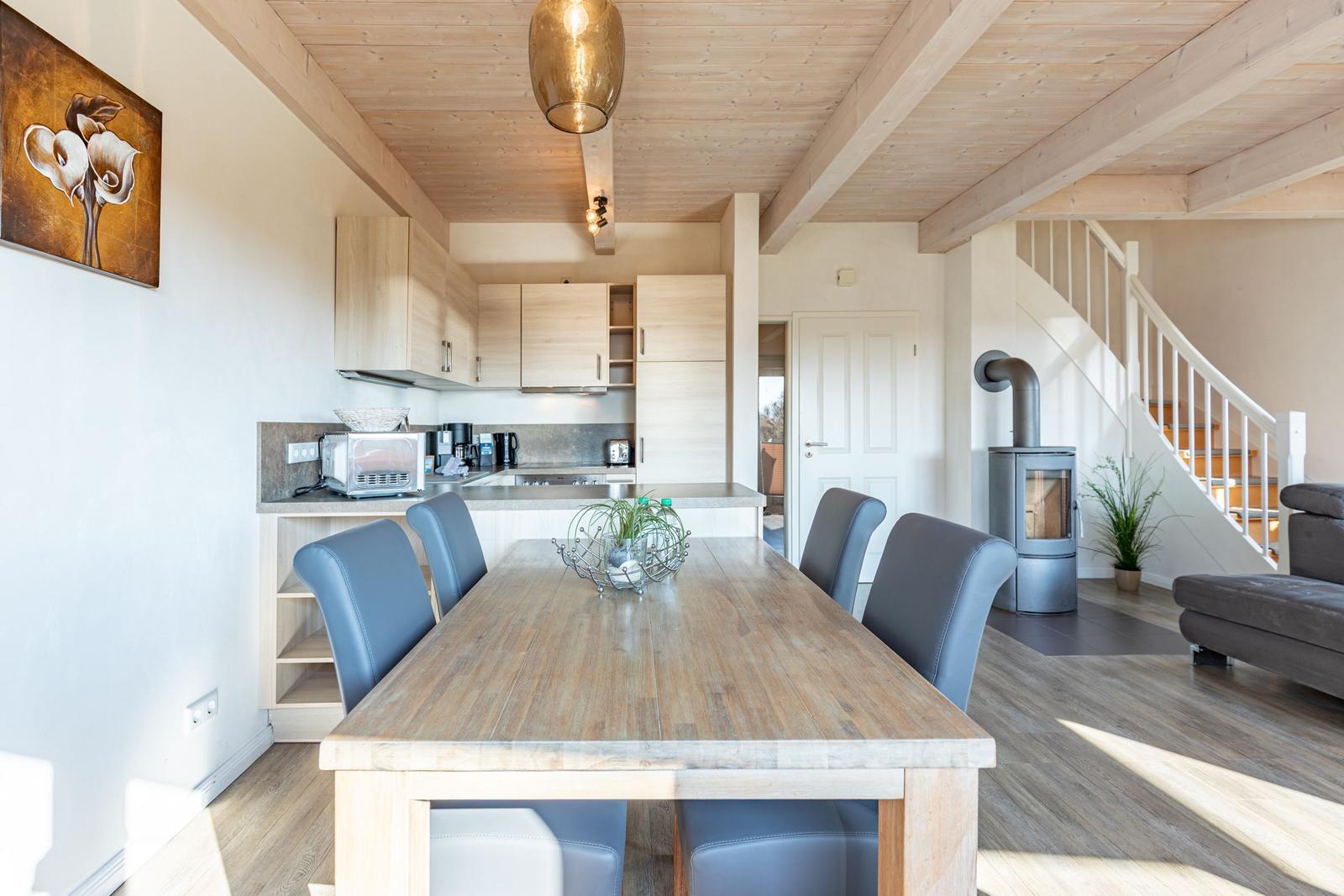 Essbereich mit Holztisch und Stühlen, Küche im Hintergrund, Holzdecke und Treppenaufgang.