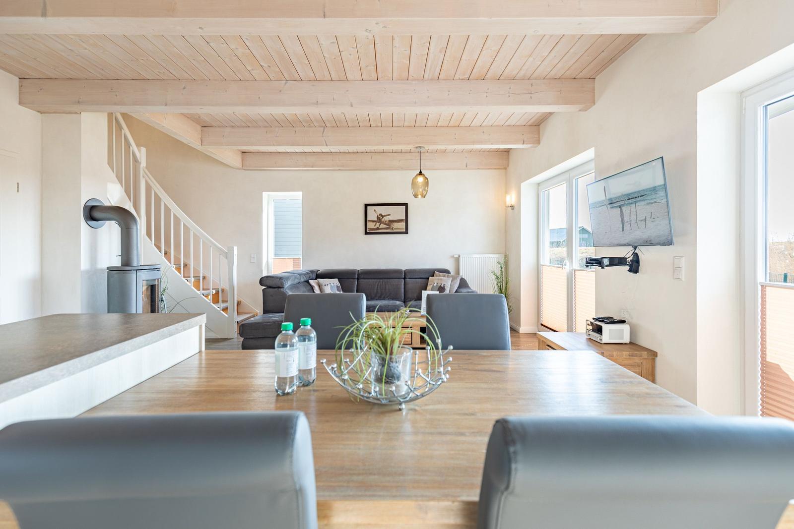 Essbereich mit Tisch und Stühlen. Im Hintergrund Wohnbereich mit Sofa und Treppenhaus.