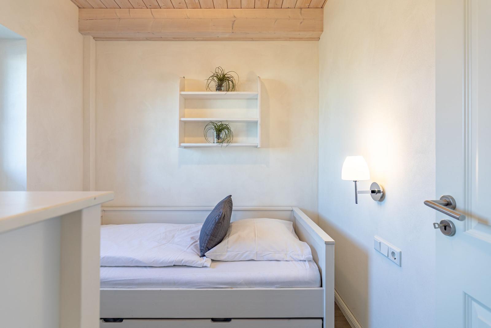 Schlafzimmer mit weißem Bett, Wandregal und Stehlampe.