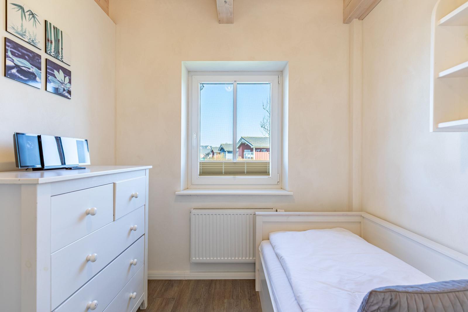 Schlafzimmer mit weißem Bett, Schrank und Fenster mit Blick auf Außenbereich.