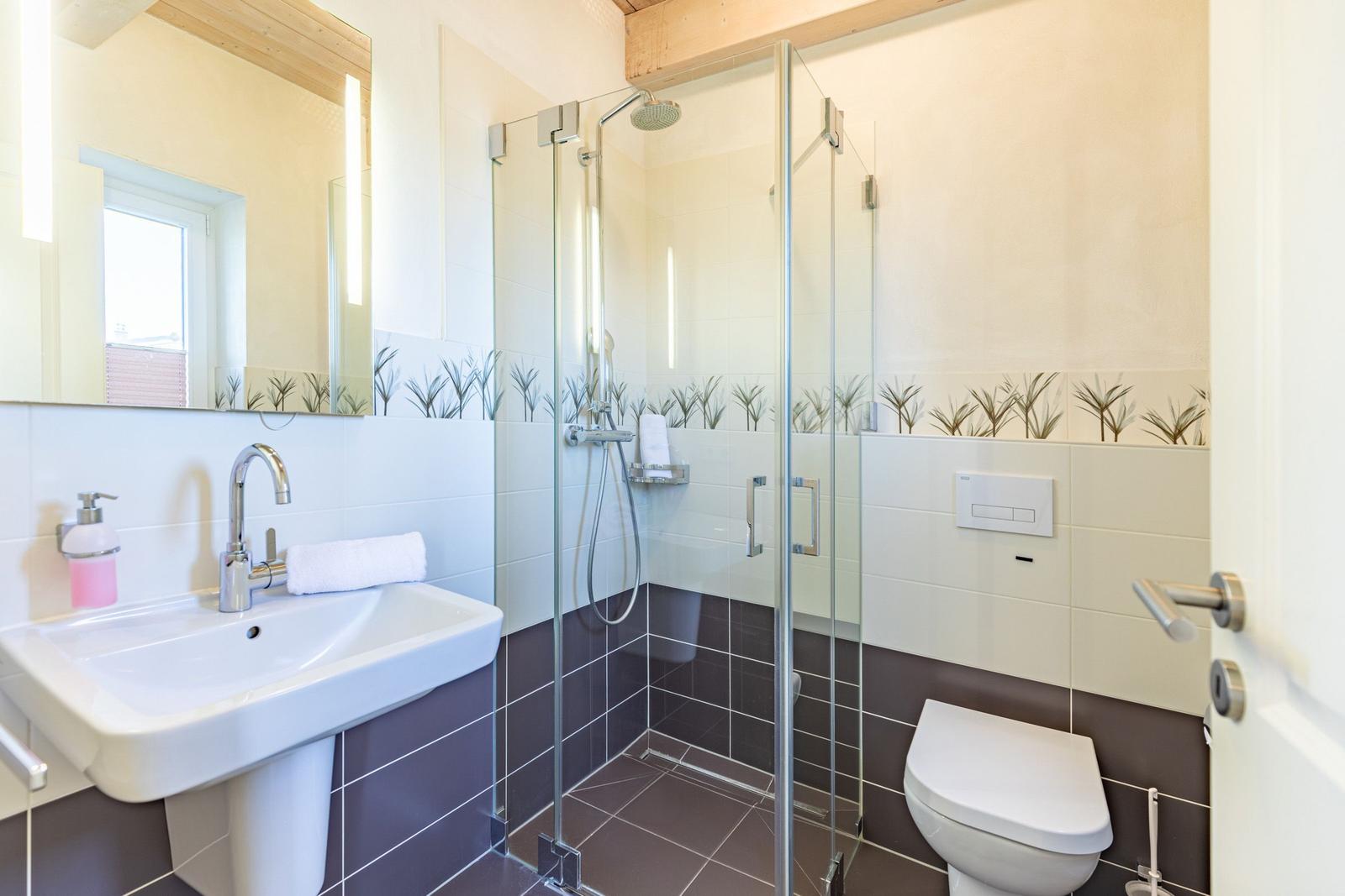 Badezimmer mit Dusche, Waschbecken und Toilette. Wandfliesen mit Pflanzenmotiv.