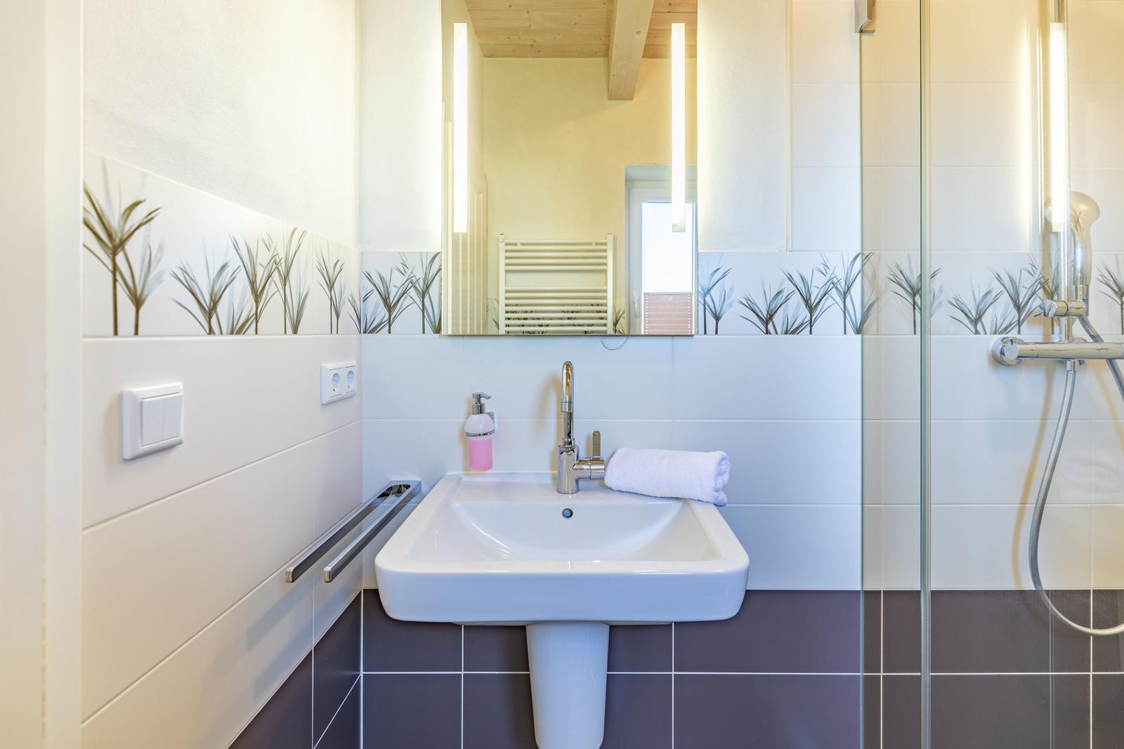 Badezimmer mit Waschbecken, Spiegel und Dusche. Wandfliesen mit Pflanzenmotiv.