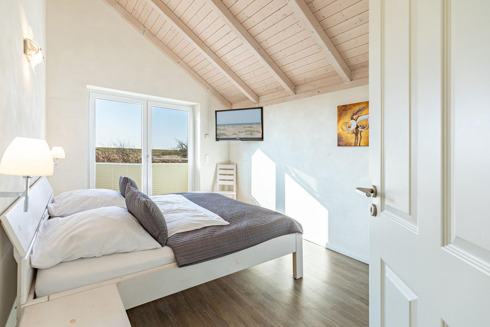 Schlafzimmer mit Doppelbett, Fenster und Holzdecke.