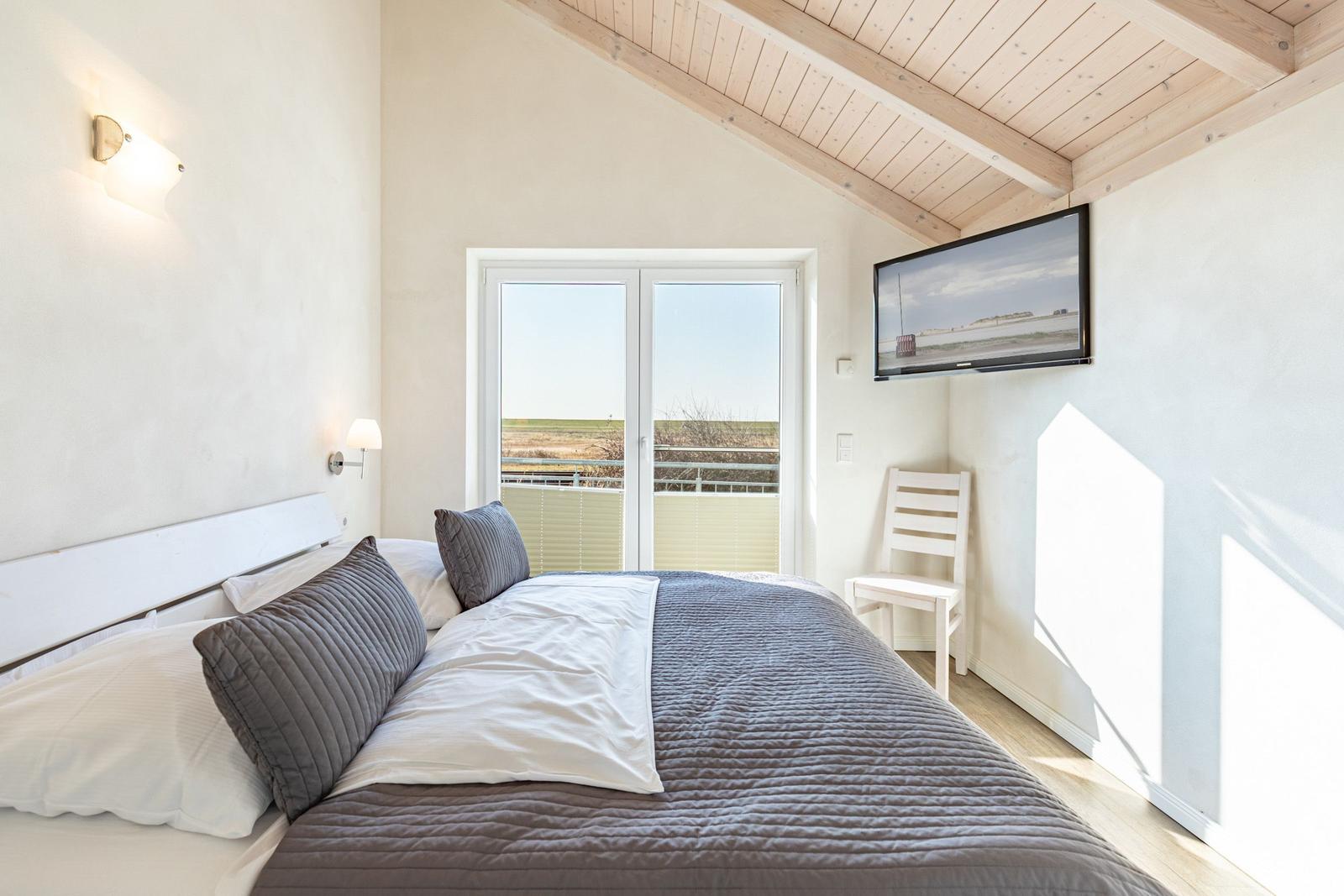 Schlafzimmer mit Bett, Fernseher und Balkontür.