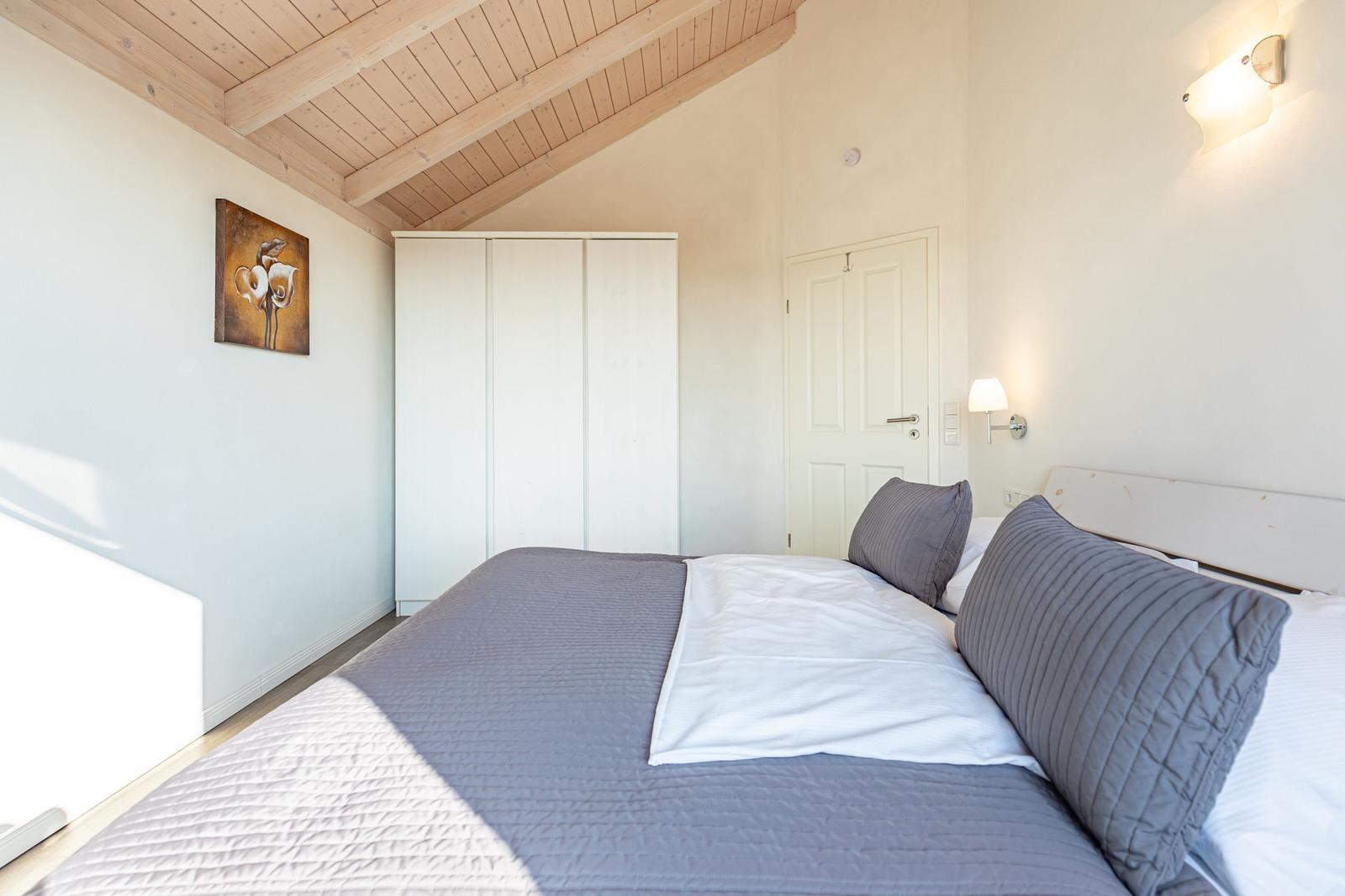 Schlafzimmer mit Bett, Kleiderschrank und Holzdecke.
