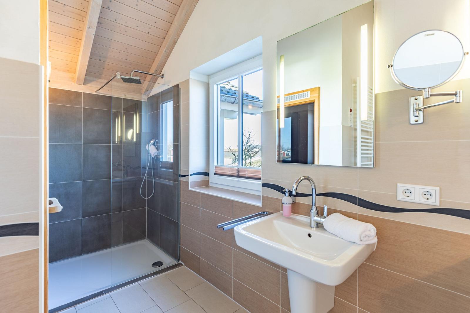 Badezimmer mit Dusche, Waschbecken und Fenster.