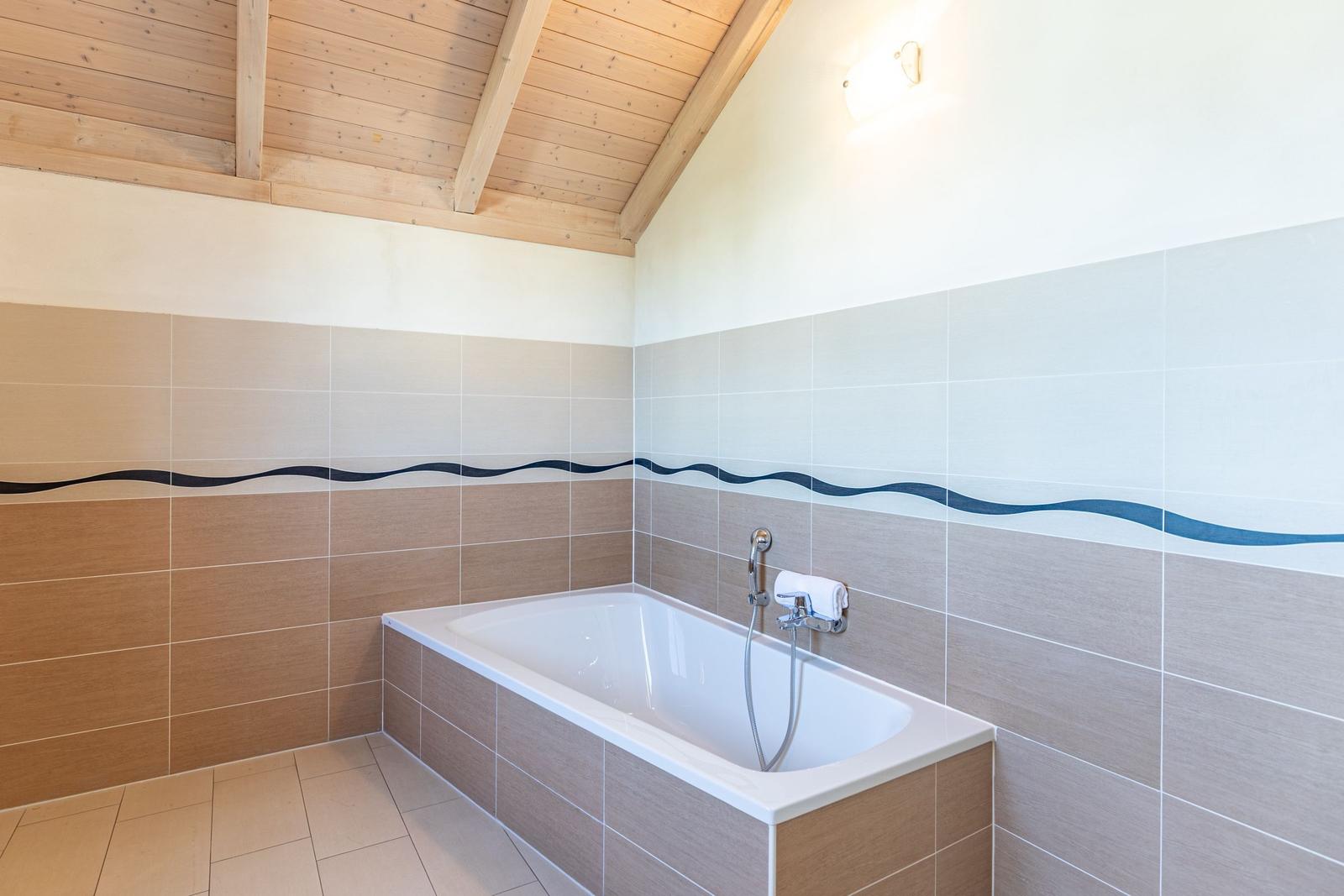 Bad mit Badewanne, gefliesten Wänden und Holzdecke