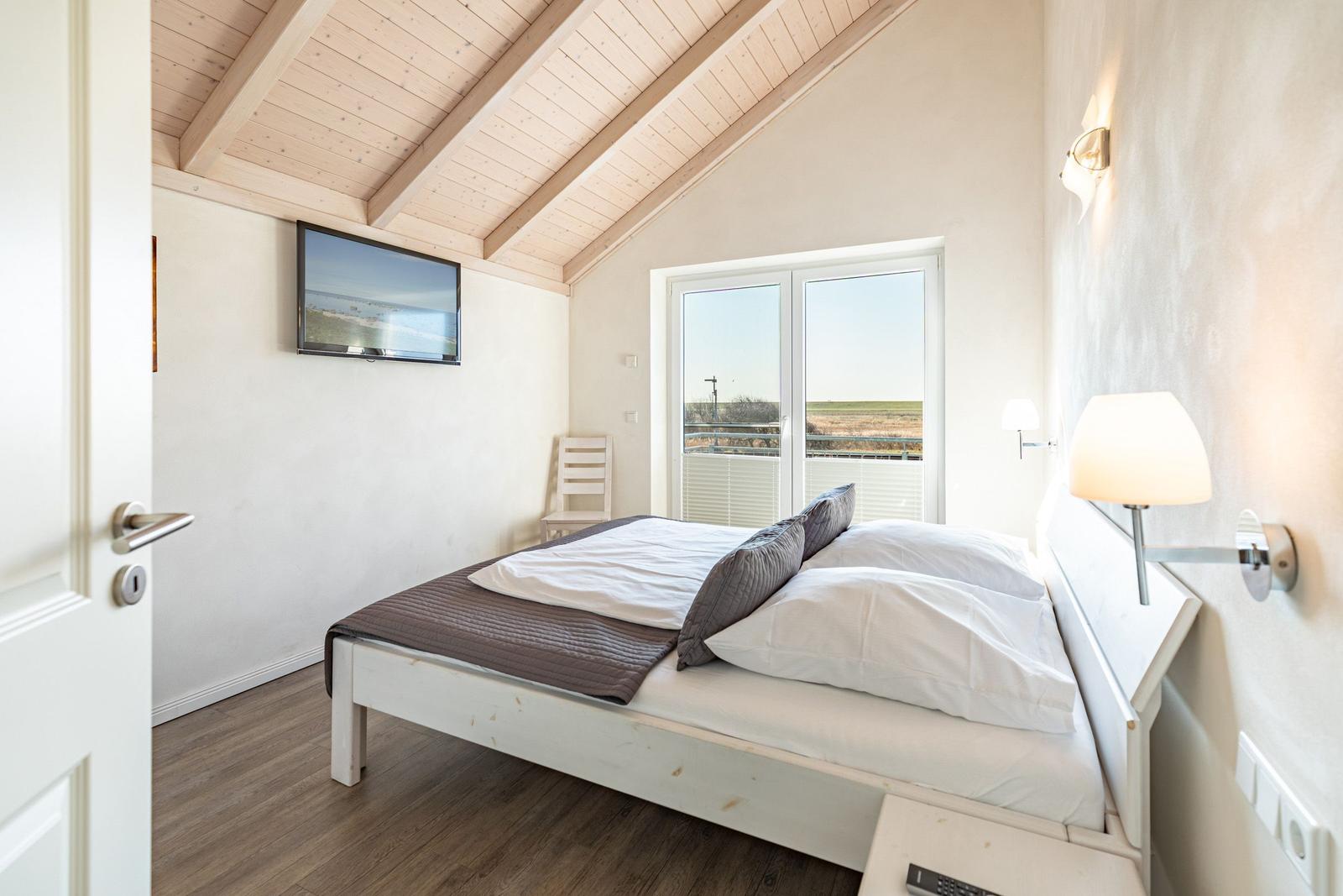 Schlafzimmer mit Dachschrägen, Bett, Fernseher und Fenster mit Blick.