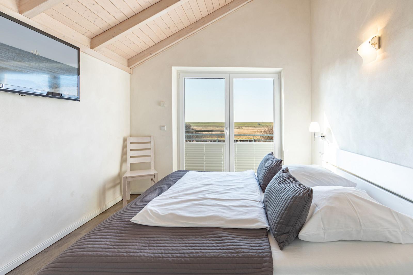 Schlafzimmer mit Bett, Fernseher und Balkon mit Aussicht.