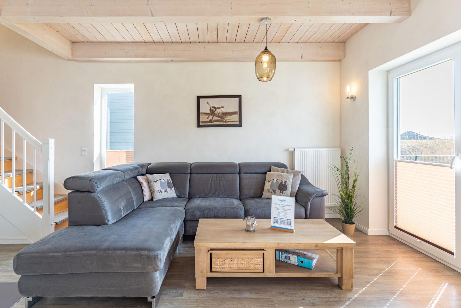 Ein Wohnzimmer mit grauem Sofa, Holztisch und Blick auf Balkon.