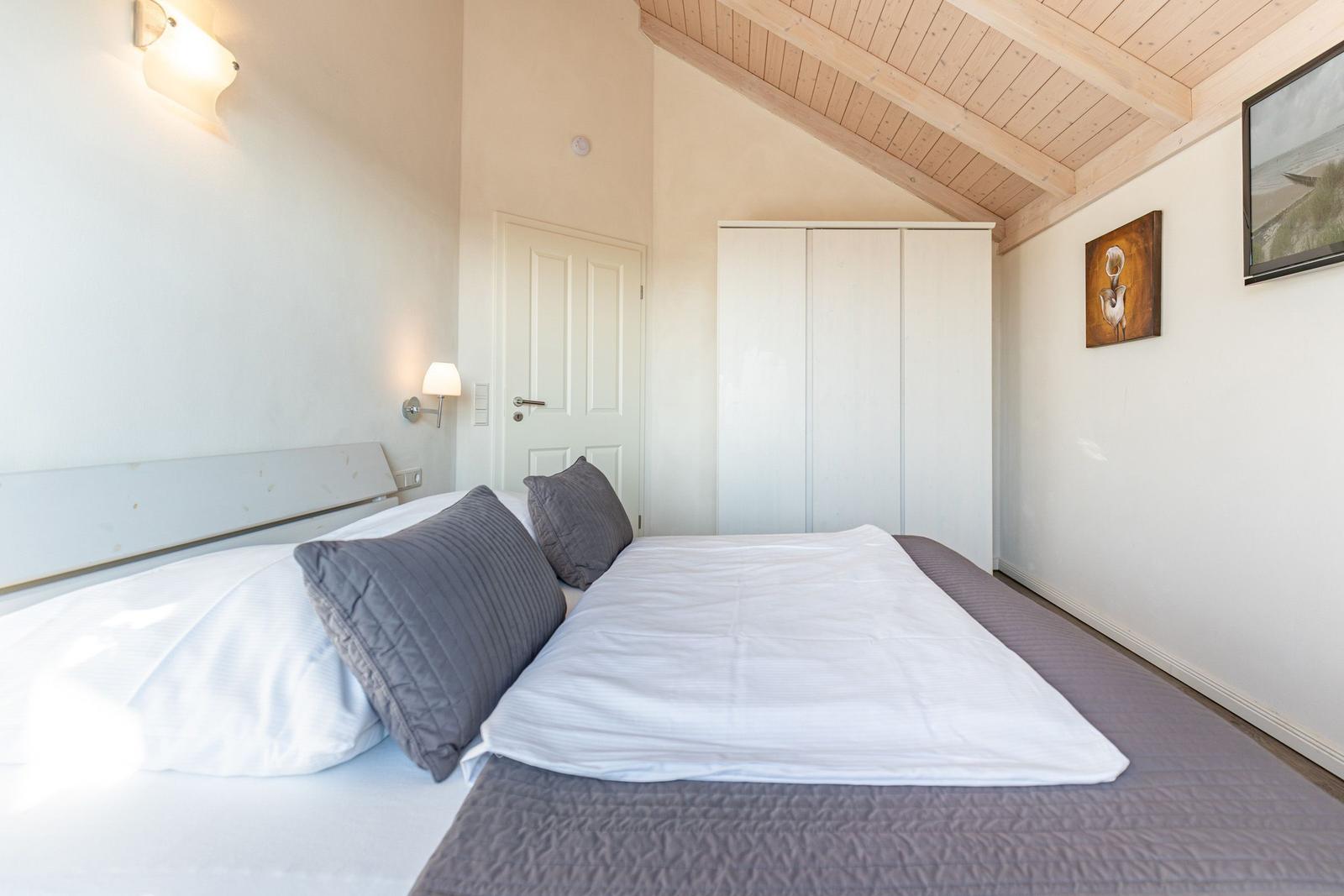 Schlafzimmer mit Doppelbett, weißen Wänden und Holzdecke.