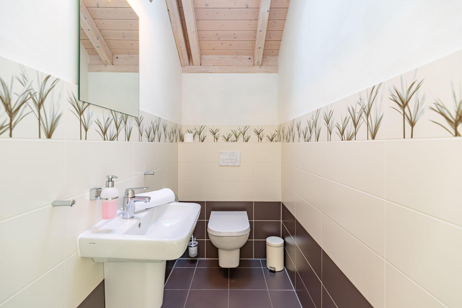 Badezimmer mit Waschbecken, Toilette und Spiegel. Wandfliesen mit Pflanzenmuster.