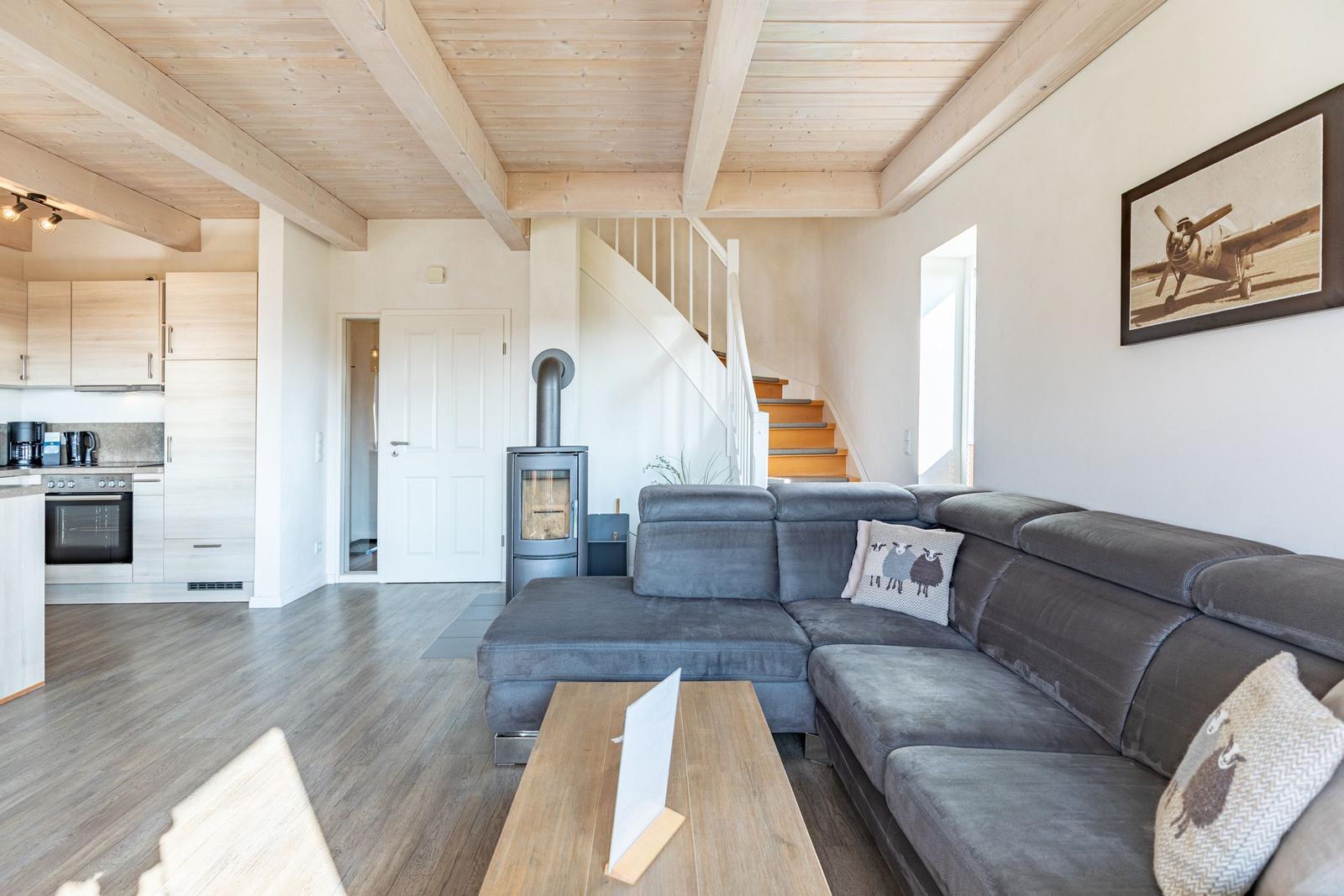 Wohnbereich mit grauem Sofa, Holzdecke und Küchenbereich im Hintergrund.