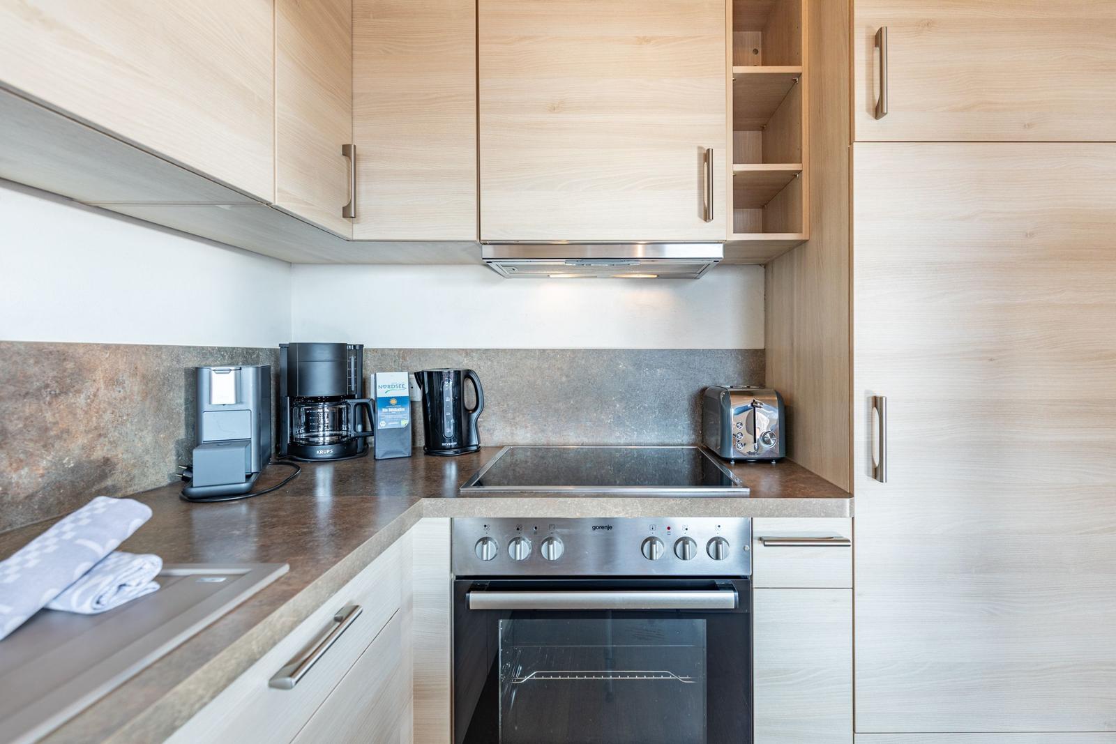 Küche mit Holzschränken, Kochfeld und Backofen sowie Kaffeemaschine und Toaster.