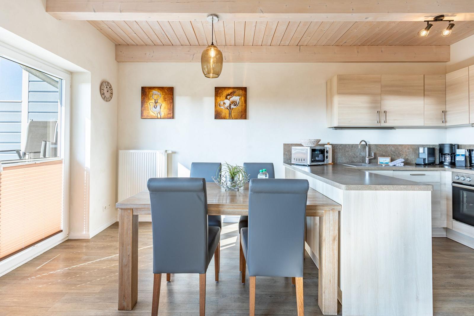 Essbereich mit Tisch, Stühlen und Kücheninsel. Holzdecke und Fenster mit Jalousie.