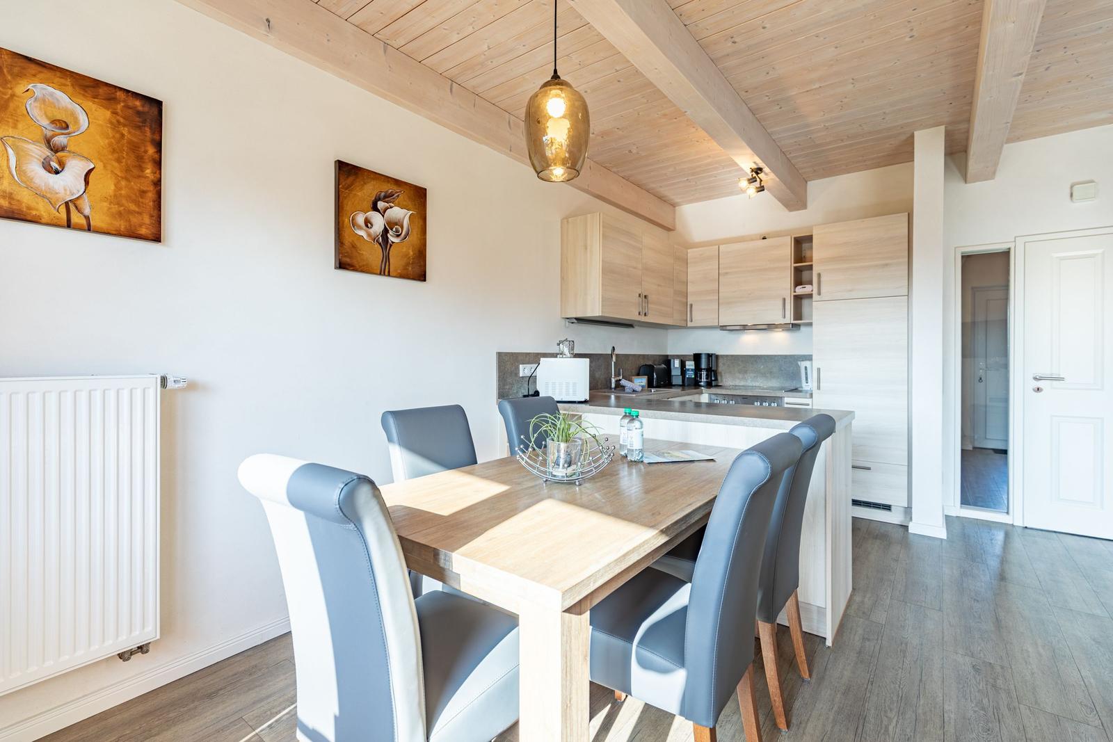 Essbereich mit Tisch, Stühlen und Küchenzeile unter Holzbalkendecke.