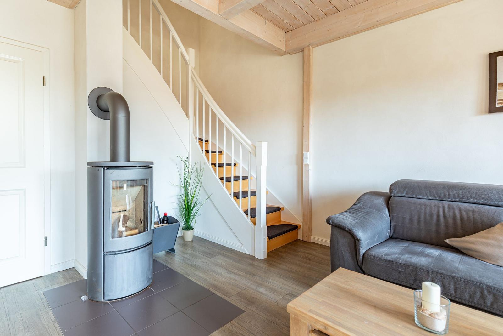 Wohnbereich mit Sofa, Kaminofen und Treppe zur oberen Etage.