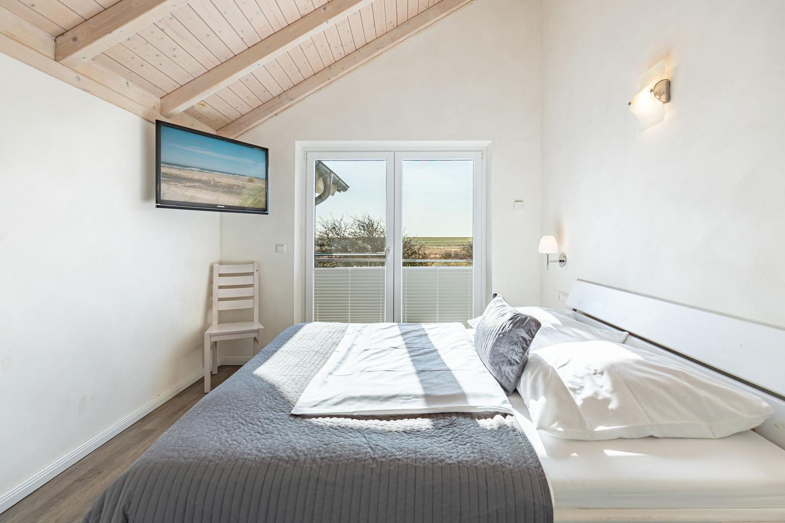 Schlafzimmer mit Bett, Fernseher und Balkonansicht.
