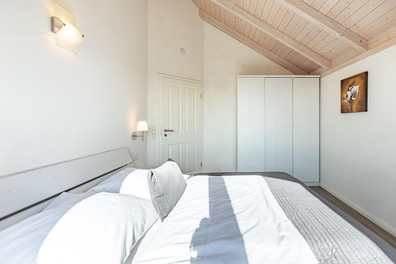 Schlafzimmer mit Bett, Kleiderschrank und Holzdecke.