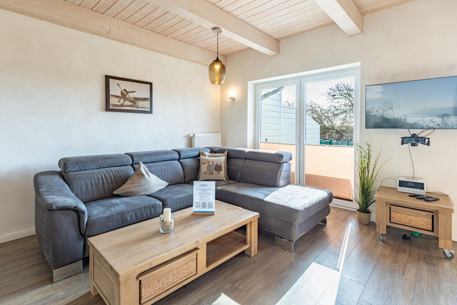 Wohnzimmer mit grauem Sofa, Holztisch und Fernseher an der Wand.