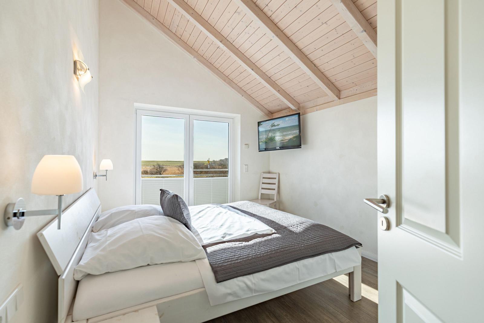 Schlafzimmer mit Dachschräge, Bett, TV und Fenster zum Blick auf die Landschaft.