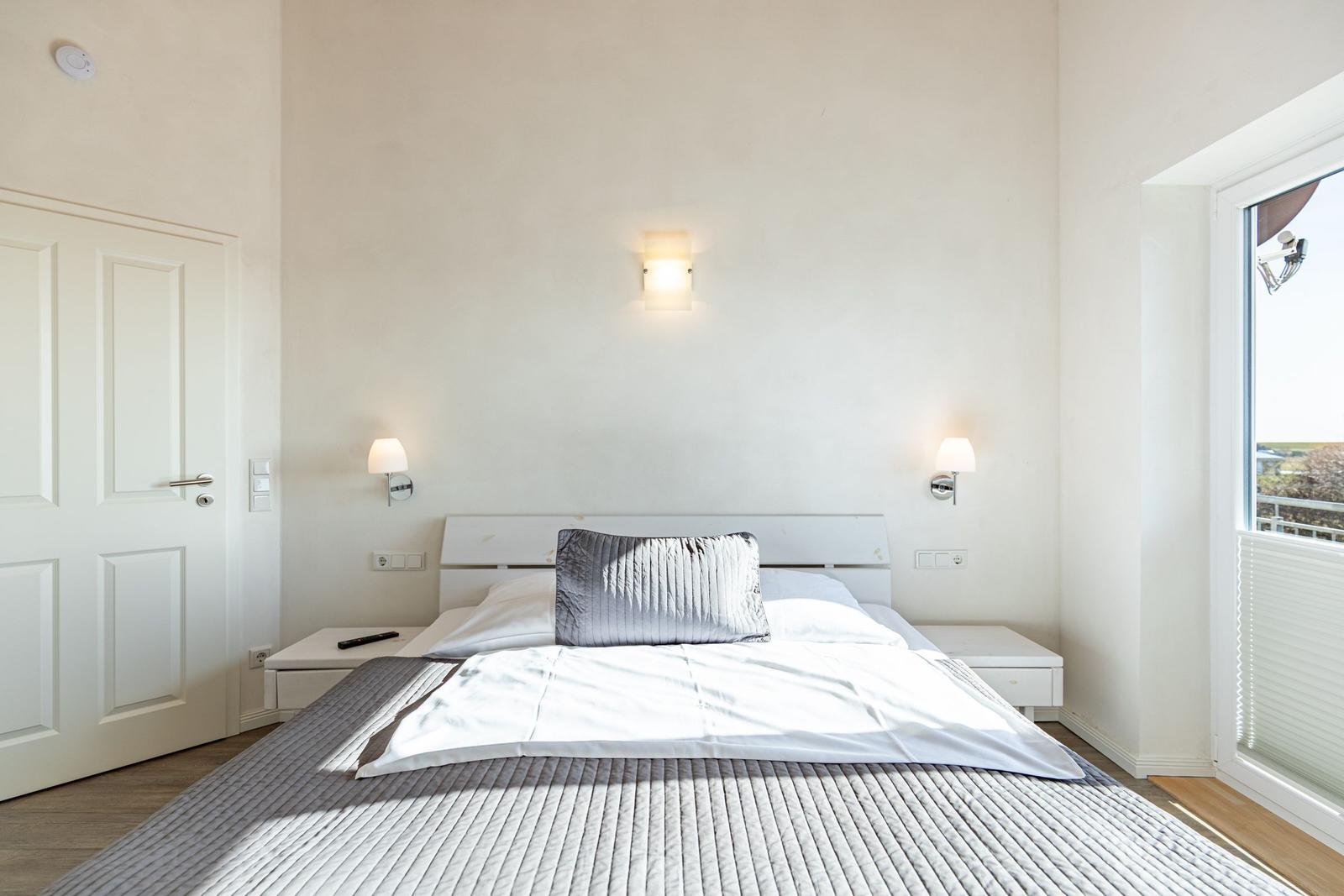 Schlafzimmer mit Bett, Nachttischen und Wandlampen. Fenster mit Blick nach draußen.
