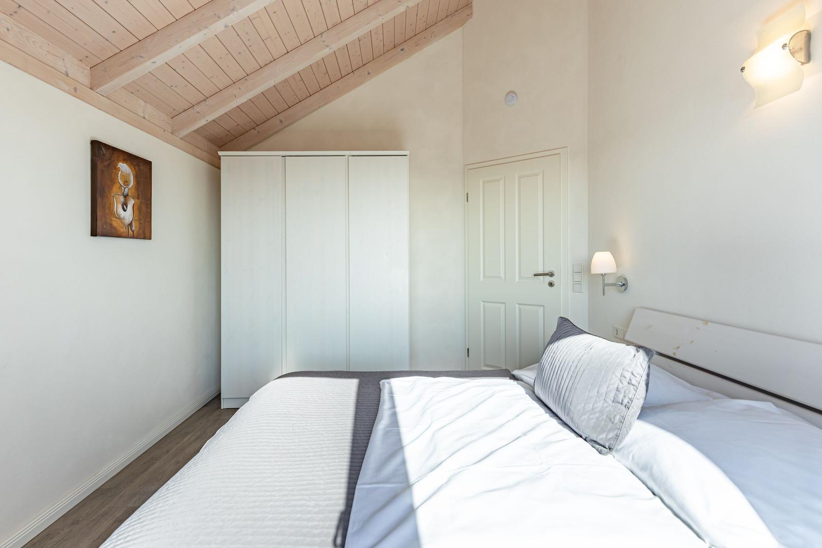 Schlafzimmer mit Bett, Kleiderschrank und Holzdecke.