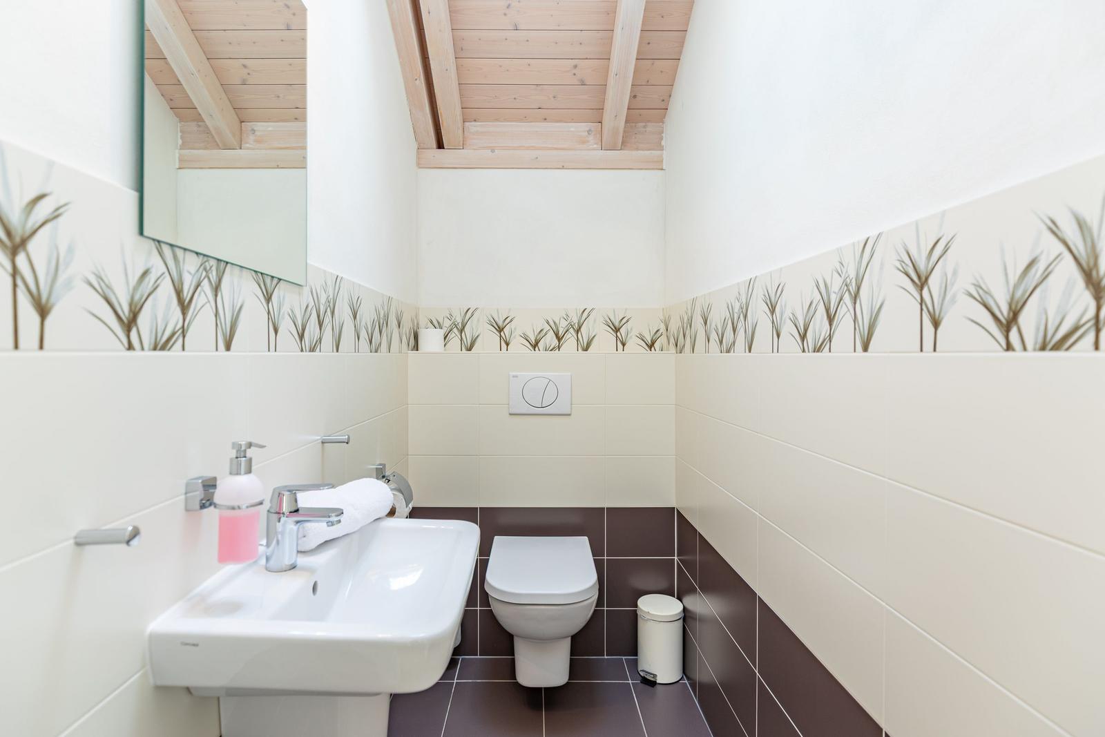 Badezimmer mit Toilette, Waschbecken und Spiegel unter Holzbalkendecke.