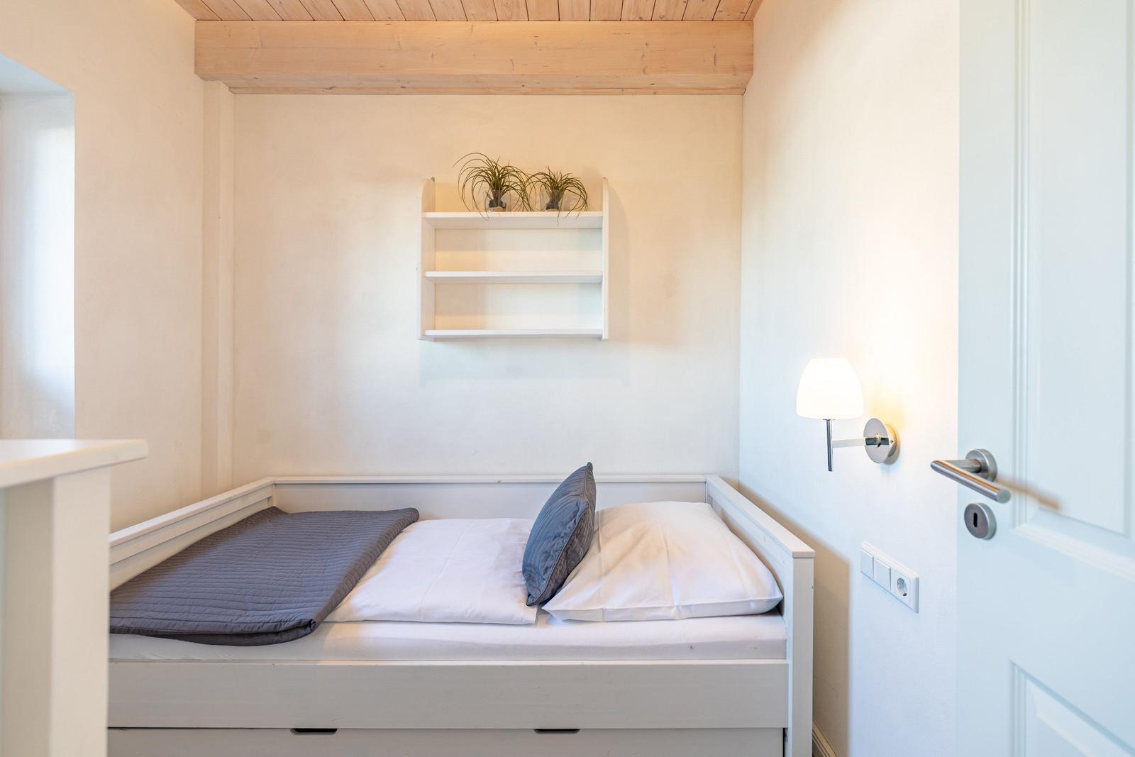 Schlafzimmer mit weißem Bett, Wandregal und Holzdecke.